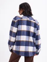 Sobrecamisa de corte holgado con estampado de cuadros en tonos azul, blanco y marrón. Presenta cierre frontal con botones, cuello clásico, bolsillos en el pecho y un interior forrado en sherpa color beige.