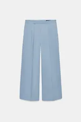Pantalón wide leg de tiro medio confeccionado en hilatura de algodón, color beige, con trabillas en la cintura, bolsillos laterales ocultos y detalle de pliegues en el delantero. Cierre frontal con cremallera, botón y ganchos metálicos.