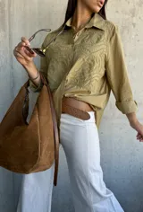 Camisa oversize de color verde oliva, con cuello clásico y cierre frontal de botones. Presenta un diseño bordado detallado en la parte superior delantera y mangas largas con puños.