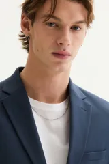 Blazer azul marino de corte slim fit, con solapas de muesca finas, botonadura sencilla de un botón visible, bolsillo superior insertado y dos bolsillos delanteros con solapa. Presenta abertura doble en la espalda y forro interior.