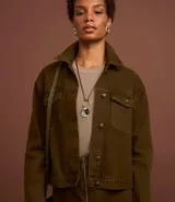 Campera trucker color verde oliva confeccionada en sarga de algodón, con cuello inglés, manga larga, bolsillos delanteros con solapa y abotonado delantero.