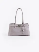 Cartera de hombro color gris, confeccionada en cuero vacuno descarne. Presenta un diseño estructurado con cierre de torniquete metálico y detalle de llavero colgante con candado y llave. Cuenta con doble asa fija.