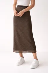Falda midi de corte recto y tiro alto, confeccionada en tejido semitransparente con estampado geométrico pequeño en tonos marrones. Presenta un detalle de encaje en la cintura y en el ruedo.