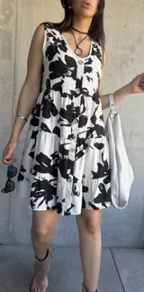 Vestido corto blanco con estampado floral negro, corte evasé, sin mangas, con botones en el frente y falda escalonada.