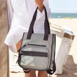 Mochila y cartera híbrida confeccionada en nylon de color beige con detalles y correas en negro. Posee dos asas superiores para llevar al hombro y correas traseras ajustables para usar como mochila. Presenta dos bolsillos frontales con cierre de cremallera y tiradores largos.