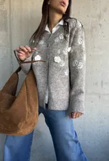 Cardigan de punto color beige con diseño de flores bordadas en relieve, cuello redondo, cierre frontal con botones y puños acanalados.