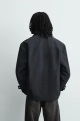 Sobrecamisa de corte relajado confeccionada en tejido efecto piel color marrón oscuro. Presenta cuello solapa, cierre frontal con botones metálicos, mangas largas con puños abotonados y dos bolsillos de plastrón con solapa en el pecho.