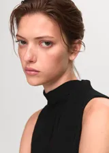 Vestido corto negro sin mangas, con cuello alto tipo halter y detalle de panel semitransparente en el frente. Presenta un diseño recto y cierre de lazo en la parte posterior del cuello.