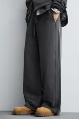 Pantalón jogger de corte wide fit confeccionado en tejido de algodón con interior de rizo. Presenta cintura elástica ajustable con cordón, bandas laterales decorativas, bolsillos laterales y un bolsillo trasero de plastrón. El acabado presenta un efecto lavado que le otorga una apariencia única.