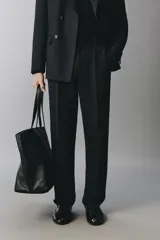 Pantalón de traje negro de corte regular fit, con pinzas delanteras, bolsillos laterales y cierre frontal con cremallera y botón.