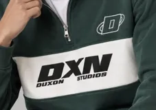 Buzo de cuello alto con medio cierre y diseño de bloques de color, verde petróleo con una franja horizontal blanca en el pecho que incluye el logo impreso en negro y detalles bordados en el pecho.