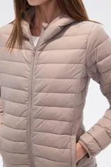 Campera acolchada tipo puffer, color beige claro, con capucha y cierre frontal. Presenta costuras horizontales y un calce entallado.