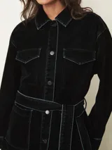 Chaqueta de terciopelo en color azul oscuro, con corte recto, cuello camisero, cierre frontal con botones metálicos y costuras a la vista en contraste. Presenta bolsillos frontales tipo parche.