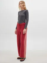 Pantalón de punto color rojo con textura efecto terciopelo, de corte ancho y holgado, con cintura elástica ajustable mediante cordón y detalle de franja lateral con patrón geométrico en tonos claros y verdosos.