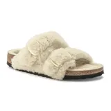 Sandalia tipo Birkenstock con doble correa forrada en corderito sintético color crema, hebillas grandes doradas y base de corcho con suela de goma negra.