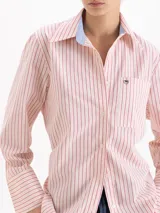 Camisa de corte holgado confeccionada en poplín de algodón. Presenta cuello clásico con interior en tela a rayas a contratono, cierre frontal con botones al tono, bolsillo plaque en el pecho con detalle de remache metálico en forma de corazón y mangas largas con puños estructurados.