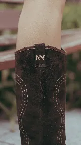 Bota alta de gamuza negra con diseño western, caña desmontable, taco ancho y detalles de tachas aplicadas.