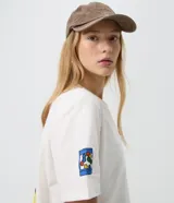 Remera blanca de algodón con cuello redondo y mangas cortas, con diseño estampado de Miffy en el pecho y detalles gráficos en la manga.