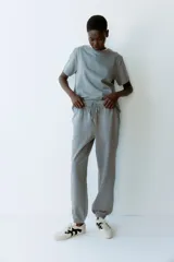 Pantalón deportivo gris de tiro alto, con cordón ajustable en la cintura elástica y bolsillos al bies. Los bajos también son elásticos y el interior es cepillado suave.