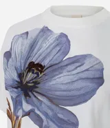 Remera de corte boxy confeccionada en algodón, con cuello redondo y mangas cortas. Presenta un estampado frontal de una flor grande en tonos violetas con detalles bordados.