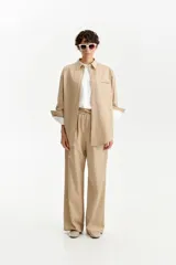 Camisa oversize de color beige claro, con cuello camisero, manga larga con puños anchos doblados y un bolsillo de parche en el pecho.