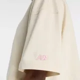 Remera cropped de algodón color crema con mangas cortas y cuello redondo. Presenta un estampado gráfico central que muestra un par de zapatillas deportivas sobre un fondo de bloques de color degradado en tonos amarillo, rosa, morado y azul.