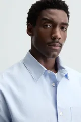 Camisa de manga larga color celeste claro, corte regular fit, con cuello solapa, bolsillo plastrón en el pecho y cierre frontal de botonadura.