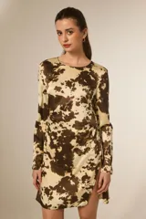 Vestido corto de poliéster satinado con estampado animal print tipo vaca en tonos marrón y beige, manga larga, cuello redondo y detalle de fruncido con abertura en la falda.