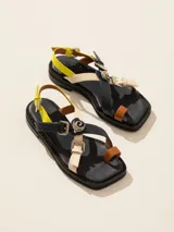 Sandalia baja de cuero vacuno con tiras cruzadas y aplique decorativo. Tiene hebilla en el talón y empeine para regular el calce.