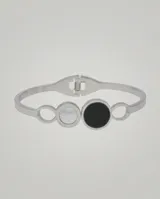 Esclava rígida de acero inoxidable con diseño de círculos entrelazados, presentando un círculo central con incrustación de nácar blanco y otro con ónix negro.