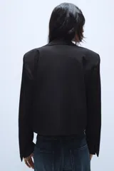 Blazer corto de corte recto con cuello de solapa, manga larga y hombreras. Presenta un diseño minimalista sin botones y forro interior a tono.