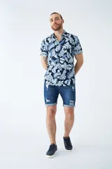 Camisa de manga corta con estampado botánico de hojas en tonos azul y blanco. Presenta cuello clásico, cierre frontal abotonado y corte slim.