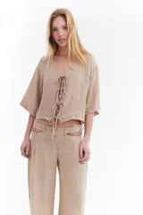 Blusa de lino italiano color beige, de manga corta, con escote en V y cierre frontal mediante lazos o moños.