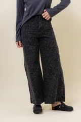 Pantalón de jean negro de pierna ancha y tiro medio-alto, con estampado sutil de leopardo en tono más oscuro y pequeños puntos blancos brillantes.