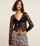 Blusa de manga larga confeccionada en encaje floral transparente, con escote en V y cierre frontal mediante lazos.
