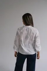 Blusa blanca de manga larga con diseño de rayas verticales y bordados florales en tono grisáceo. Presenta cuello camisero, cierre frontal con botones y puños elásticos.