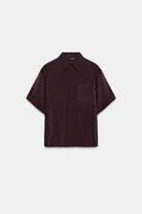 Camisa de manga corta con cuello solapa, confeccionada en tejido fluido con acabado satinado. Presenta un bolsillo frontal, cierre con botones ocultos y mangas con dobladillo.