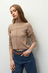 Polera blanca de manga larga con cuello alto y costuras cruzadas a la vista en el frente.