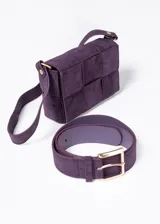 Set de cartera bandolera y cinto de poliéster color violeta. La cartera tiene diseño tejido y correa larga. El cinto tiene hebilla dorada.