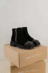 Bota corta de cuero gamuzado color marrón chocolate, con punta cuadrada y suela track. Presenta una correa con hebilla desmontable y cierre lateral con cremallera.