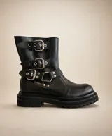 Bota de caña media confeccionada en cuero natural, con suela track de goma y diseño robusto. Presenta tres correas ajustables con hebillas metálicas y detalles de remaches plateados, aportando un estilo motero y moderno.