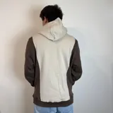 Canguro con capucha de diseño bicolor, combinando paneles en color blanco y beige. Presenta un bolsillo frontal tipo canguro y el logo de la marca bordado en el pecho.