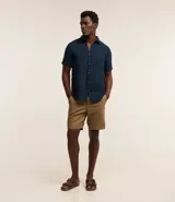 Bermuda básica masculina confeccionada en sarga de algodón, de corte recto con trabillas en la cintura, bolsillos y cierre frontal con botón y cremallera.