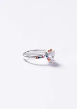 Anillo de plata 925 con diseño de corazón central compuesto por una zirconia transparente, rodeado por pequeñas piedras multicolor. El cuerpo del anillo también presenta incrustaciones de piedras en tonos variados a lo largo de la banda.