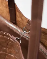 Cartera grande marrón de símil cuero con textura efecto cocodrilo, diseño estructurado tipo tote con doble asa larga de hombro y detalles de tiras laterales.