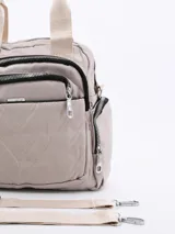 Cartera tipo mochila de color beige, confeccionada en material sintético con diseño acolchado de costuras en forma de V. Cuenta con múltiples compartimentos frontales con cierre, asas superiores y correas ajustables para llevar en la espalda.