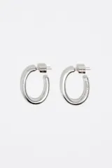 Caravanas de aro con diseño ovalado y acabado metálico plateado. Poseen un cuerpo tubular grueso, cierre de presión y detalle de grabado en uno de los laterales.