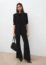 Blazer negro de corte sastrero, con solapas clásicas, cierre frontal de un botón y bolsillos laterales con solapa. Presenta un diseño estructurado con hombreras y forro interior.