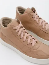 Botín de cuero color nude, con caña alta, cordones y suela blanca.