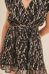 Vestido corto con escote en V profundo y mangas cortas estilo kimono. Presenta un estampado floral con hilos metalizados dorados sobre fondo negro y un ruedo con volado. Incluye forro interior.